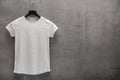 Front side of female grey melange cotton t-shirt on a hanger and a concrete wall in the background Royalty Free Stock Photo