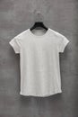 Front side of female grey melange cotton t-shirt on a hanger and a concrete wall in the background Royalty Free Stock Photo