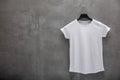 Front side of female white cotton t-shirt on a hanger and a concrete wall in the background. T-shirt without print and copyspace f Royalty Free Stock Photo