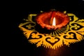 Front side of glowing terracotta lamp placed on yellow rangoli and black background. diwali concept