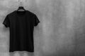 Front side of male black cotton t-shirt on a hanger and a concrete wall in the background