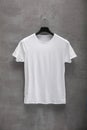 Front side of male white cotton t-shirt on a hanger and a concrete wall in the background Royalty Free Stock Photo