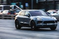 Front side view of gray Porsche Macan fast moving on the city road. Car rushing on speedway. SUV driving along the street with