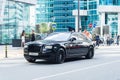 Front side view of a very expensive premium Rolls Royce Ghost car, luxury black saloon. Background of modern office buildings