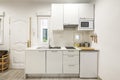 Front of a small kitchen with white cabinets with matching appliances and a small window in one corner Royalty Free Stock Photo