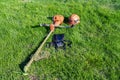 Front up view at handheld gasoline lawn mower, safety helmet with eye and hearing protection, padded shoulder straps left after