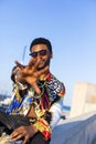 Front view of a african american bearded young man wearing sunglasses sitting in a fence while hiding against the hand in a sunny