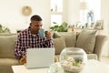 Man drinking coffee while using laptop on sofa in living room Royalty Free Stock Photo