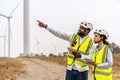 Front view of african american man and woman engineers in uniform discuss and use tablet working stand near wind turbines