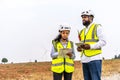 Front view of african american man and woman engineers in uniform discuss and use tablet working stand near wind turbines