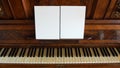Front view of an antique piano with the keyboard open and two sheets of blank paper on support for musical notes Royalty Free Stock Photo