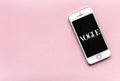 Front view of Apple iPhone with text of Vogue on the screen. Phone on pink background. Beauty flat lay