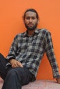 Front view of a attractive bearded young man looking at camera, sitting against orange wall background with copy space Royalty Free Stock Photo