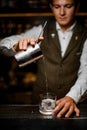 front view of bartender gently pouring drink from mixing cup with strainer