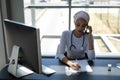 Beautiful mixed-race female doctor talking on mobile phone while writing on clipboard Royalty Free Stock Photo