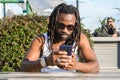 front view of black man with dreadlocks sitting outdoors watching his phone attentively Royalty Free Stock Photo