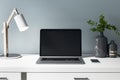 Front view on blank black laptop display on white table with stylish vase, lamp and smartphone. Mockup