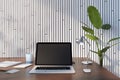 Front view on blank dark modern laptop monitor with blank place on brown wooden table with notebooks and coffee mug on green plant