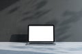 Front view on blank white laptop screen with space for your logo or text on light grey concrete surface and dark sunlit wall