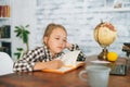 Front view of bored tired cute elementary child school girl doing writing homework holding pen sitting at table with Royalty Free Stock Photo