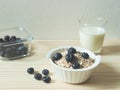 Breakfast with oat or granola in white bowl, fresh blueberries, glass of milk on wooden table. Healthy breakfast concept