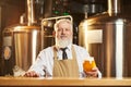 Front view of brewer standing over bar with glass of beer