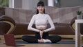 Front view calm confident female yogi sitting in lotus pose meditating inhaling and exhaling in slow motion. Wide shot