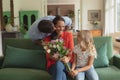 Daughter giving bouquet to mother while father kissing her in living room Royalty Free Stock Photo