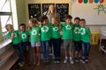 Female school teacher with a group of schoolchildren wearing green t shirts with a white recycling l