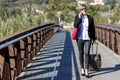 Front view of the cheerful business woman carrying the luggage while holding a red shoulder bag and talking by phone Royalty Free Stock Photo