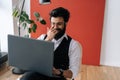 Front view of cheerful Indian business man in formalwear working on laptop sitting on chair in light coworking office. Royalty Free Stock Photo