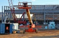 Front view of cherry picker. On background a building under construction and several machinery and men at work