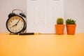 front view. clock, calendar and plant placed on yellow table background with copy space. image for