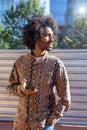 Front view of a cool young smiling afro man using a mobile phone while standing outdoors in a sunny day Royalty Free Stock Photo