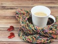 Front view of cup of latte coffee  wrap in colorful scarf and two red glitter hearts on wooden table Royalty Free Stock Photo