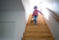 A cute small girl walking down wooden stairs indoors at home.