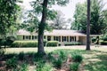 Front view of exterior white cream brick 1950`s house with black shutters and a large lawn