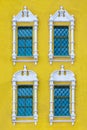 A facade of ancient yellow building with four windows with carved white stone platbands  as texture vertical Royalty Free Stock Photo