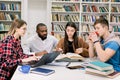 Front view of four good-looking modern smart mixed race students which are sitting in the reading room of library and