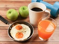Front view of fried eggs in pan , orange juice , apples , black coffee and blue dumbbells on wooden background Royalty Free Stock Photo