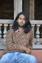 Front view of a good looking Indian young man with long hair style, looking at camera while sitting on temple stairs Royalty Free Stock Photo