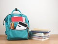 Front view of green backpack with school supplie, stack of books on wooden table and white background with copy space Royalty Free Stock Photo