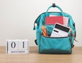 Front view of green backpack with school supplies and wooden calendar September 01 on wooden table and white background with Royalty Free Stock Photo