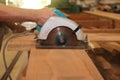 Front view of hands of senior carpenter cutting a piece of wood against electric circular saw in carpentry woodshop. Woodworking c