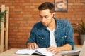 Front view of handsome focused young man reading business paper book sitting at desk with laptop at home office. Royalty Free Stock Photo