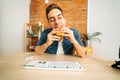 Front view of handsome hungry young man eating hamburger with beef from fast food restaurant sitting at desk with Royalty Free Stock Photo