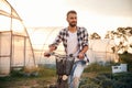 Front view. Handsome man in casual clothes is with bicycle on the agricultural field near greenhouse Royalty Free Stock Photo