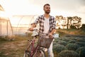 Front view. Handsome man in casual clothes is with bicycle on the agricultural field near greenhouse Royalty Free Stock Photo