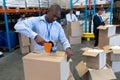 Male staff packing cardboard box with tape gun dispenser in warehouse Royalty Free Stock Photo