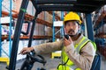 Male worker talking on walkie-talkie while driving forklift in warehouse Royalty Free Stock Photo